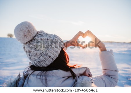 happy young woman hiking in snowy mountain at sunset doing a heart shape with hands. winter season. nature and love Royalty-Free Stock Photo #1894586461