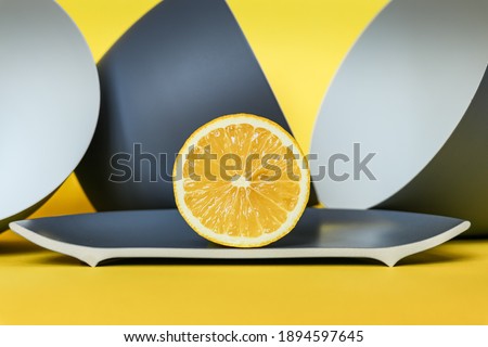 Still life with half a lemon and gray matte dishes on a yellow background