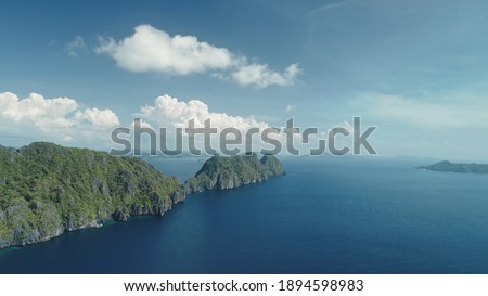 Hilly islands at blue ocean coast aerial view. Nobody nature scenery of Palawan, El Nido Isles, Philippines. Green tropic forest at mount ranges under fluffy clouds on sky. Cinematic drone shot