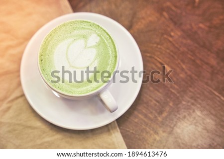 Cup of matcha latte on wooden background and a beige napkin in a cafe with copy space. High quality photo