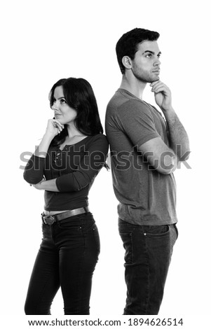 Studio shot of young couple standing while thinking and looking up together with back to back
