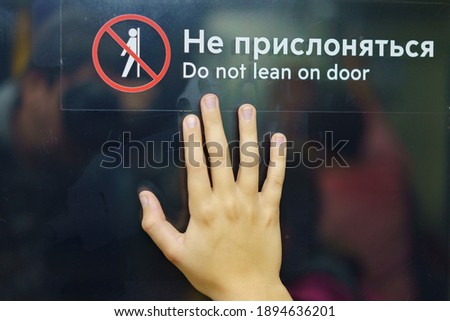 The sign: Do not lean on door (translation). A human palm leaned against the door with the words Do not lean.