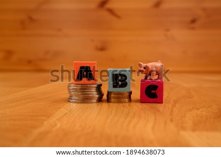 Colorful worn plastic cubes forming the word ABC. Stacks of coins with a miniature pig. Concept of economical planning. Close up and isolated against a wooden background.