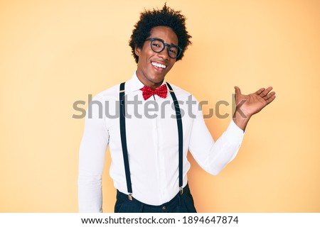 Handsome african american man with afro hair wearing hipster elegant look smiling cheerful presenting and pointing with palm of hand looking at the camera. 