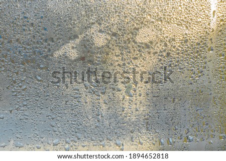 Raindrops on the glass in rainy weather.The glittering, shiny surface of water on glass.Water drops in the form of balls or spheres.Grey raindrops background. Abstract backgrounds ornament with water