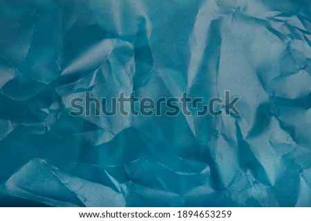 Close up picture on a blue colored plastic transparent cellophane bag on white background. The plastic has a shiny texture and the surface is wrinkly and tattered making abstract pattern. 