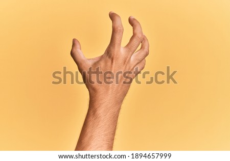 Arm and hand of caucasian man over yellow isolated background grasping aggressive and scary with fingers, violence and frustration  Royalty-Free Stock Photo #1894657999