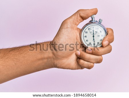 Hand of young hispanic man using stopwatch over isolated pink background. Royalty-Free Stock Photo #1894658014
