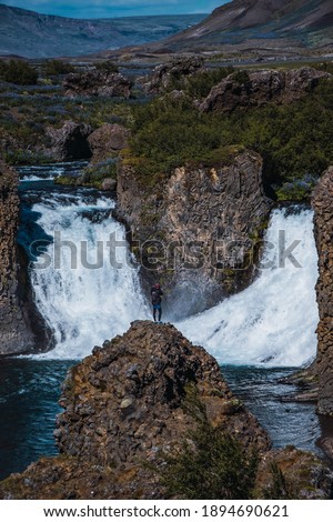 Man in a rock taking a picture of two waterfalls in Iceland