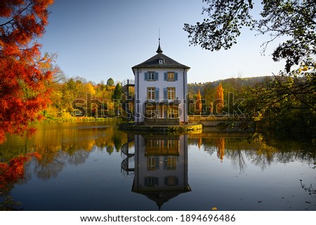 A baroque house, called Trappenseeschlösschen, surrounded by Lake Trappensee in Heilbronn, Germany during autumn. The house and the colorful trees reflect in the water. Royalty-Free Stock Photo #1894696486