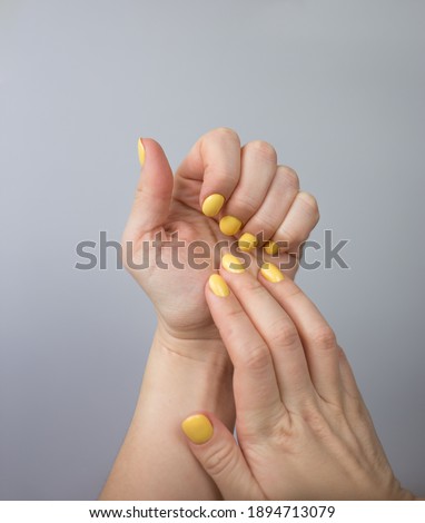 Hands close up with manicure in yellow. Colors of the year 2021- yellow and ultimate gray background.