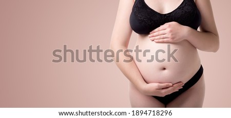 Belly of pregnant woman with hands holding tummy, health care matherhood close up on a gradient beige background.