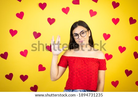 Young beautiful woman over yellow background with red hearts doing hand symbol