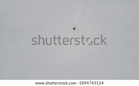 Aerial drone shot of lone snow school runner in white empty winter landscape