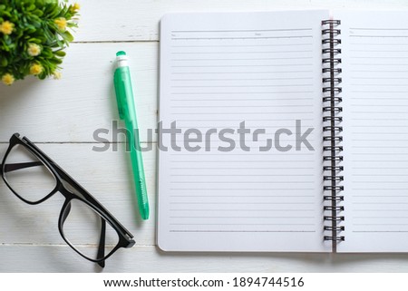 White wooden table with note book, eyeglasses, pen, decorative plants. Top view with copy space, flat lay.