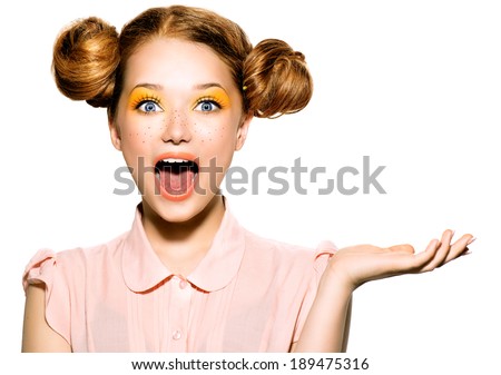 Beauty Surprised Teenager Model Girl. Beautiful Joyful teen girl with freckles, funny red hairstyle and yellow makeup. Open hand. Professional make up. Isolated on a white background