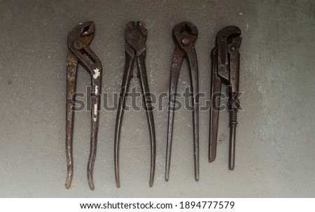 Four old rusty tools over gray concrete floor. Gripper, wrench, tong and cutter on grunge background.
