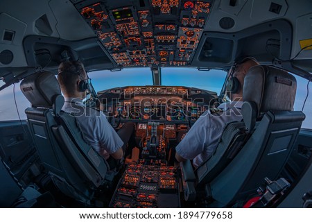 Pilots in the cockpit of jet commercial airplane during the flight with first rays of the warm sunrise entering through the flight deck window Royalty-Free Stock Photo #1894779658