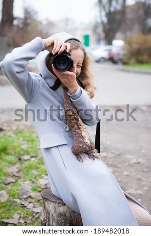 Young girl press photographer or tourist shooting looking at us against the blurred background in city