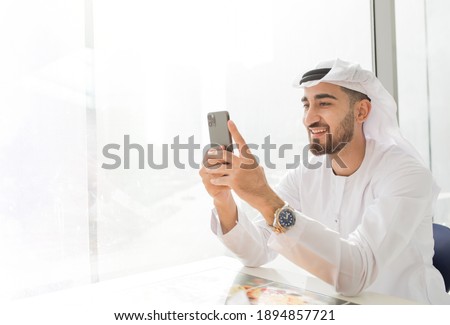 Arabic corporate business man wearing kandora looking at mobile phone and smiling - Portrait of traditional Emirati man Royalty-Free Stock Photo #1894857721
