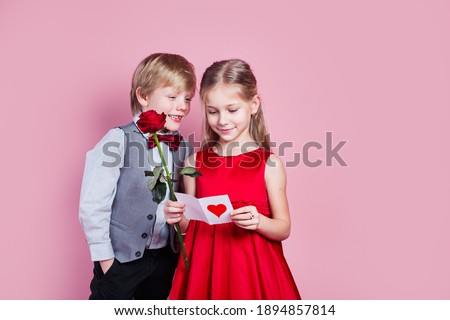 Valentines day. Cute six year old girl with a Valentine's card in her hand and funny little boy on pink background