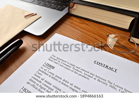 "There is a dummy paper of Contract
 on the desk with a laptop, a pen and glasses."