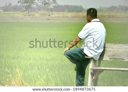 Behind shot of man in white shirt sitting alone on edge of bench and thinking something about life of himself.