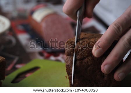 A young man makes a sandwich of black bread and sausage.
