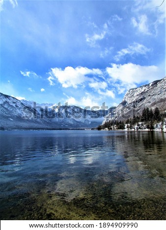 Scenic winter view of Bohinj lake in Gorenjska, Slovenia with a reflection of the mountains and clouds in the lake and mountains of the Julian alps behind