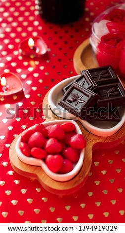 Chocolates and sweets on heart-shaped plates. Festive table setting for date of lovers. Red background. Vertical photo