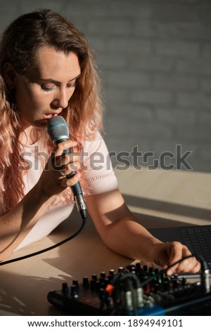 A woman sings into a microphone and plays online. A female blogger is recording a song using a synthesizer with a laptop.
