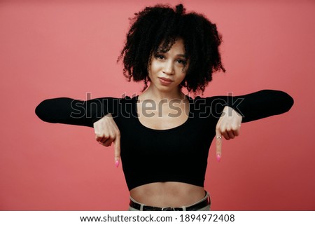 makes a downward gesture with her hands, a young Afro-ethnic woman. A model in a photo studio poses on a scarlet background.