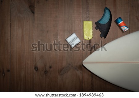 Surf board and accessories (wax, fin, sunscreen and spatula) on wood background