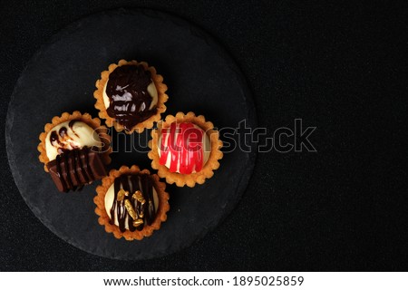 Flatlay picture of 4 type homemade cheese tart on slate plate at copyspace dark background.