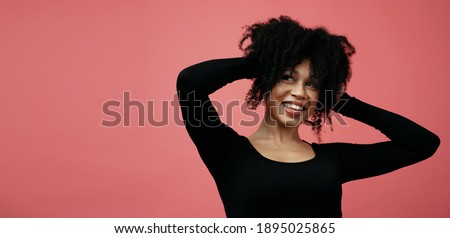 dancing and rejoicing holding his hands near his hair. the young woman is Afro-ethnic. A model in a photo studio poses on a scarlet background.