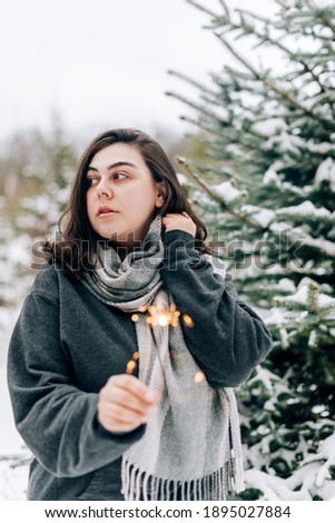 Adult young woman with sparklers on the background of winter pine forest