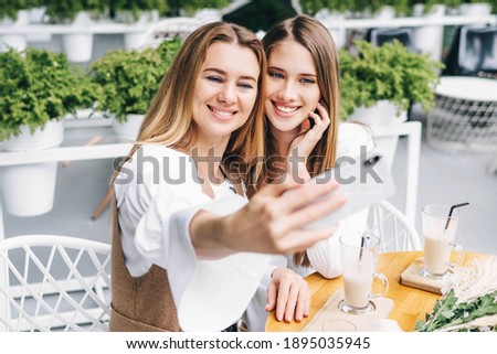 A beautiful mother and daughter spend time together. Take a selfie on the summer terrace in a cafe.