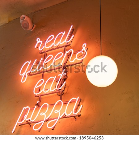 Glowing light neon "real queens eat pizza" hanged on wall near sphere lamp