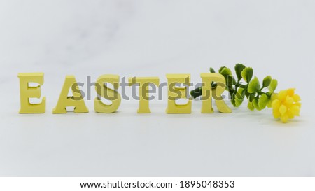 Word Easter from yellow wooden letters and flower on white marble background. Postcard, banner for congratulations with Easter. Minimalistic blank for design. Selective focus, blurred background