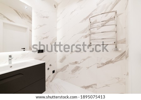 bathroom with light tiles, black bedside table under the carcass and mirror as it glows