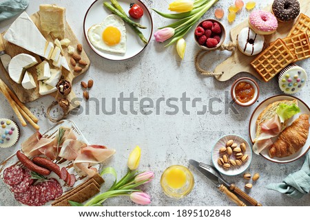  Breakfast food table. Festive brunch set, meal variety with grill platter, fried egg, croissant sandwich, cheese platter and desserts. Overhead view