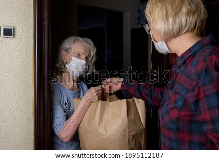 An older masked woman receives a bag of food from volunteer neighborhood help Royalty-Free Stock Photo #1895112187
