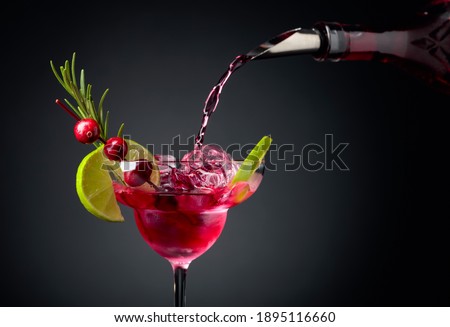 Cranberry cocktail garnished with berries, lime, and rosemary. In frozen glass with ice is pouring cranberry liquor. Copy space.