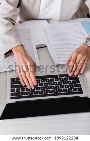 partial view of translator typing on laptop near documents in office