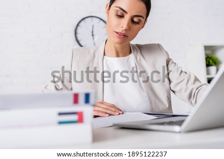 focused translator working near laptop and dictionaries of french and arabian languages on blurred foreground