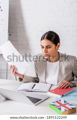 concentrated translator holding document near empty notebook and laptop