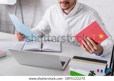 partial view of translator holding chinese dictionary near notebook and laptop