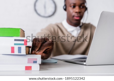 african american translator in headset taking dictionary while working at laptop, blurred background