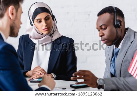 arabian and african american business people in headsets near digital translators and interpreter on blurred foreground Royalty-Free Stock Photo #1895123062