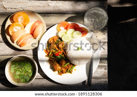 Stir fried chicken and sting bean red curry paste serve with seasonal fruit soup and drinking water on wooden table in high contrast lighting stock photo